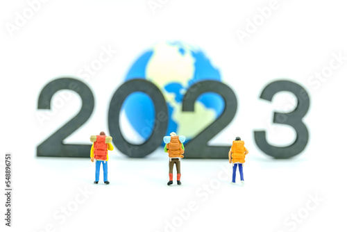 2023 New Year and Travel Concept. Group of traveler miniature figures with backpack standing with wooden number block with mini world ball on white background.