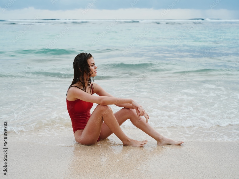 Woman with wet hair after swimming in the ocean in a red bathing suit on Bali beach, a trip to Indonesia for the winter