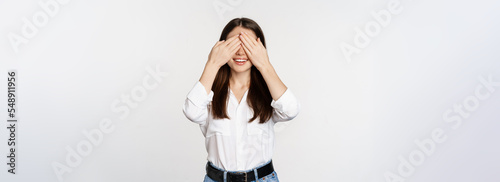 Smiling happy woman waiting for surprise, shut eyes with hands, standing blindsided against white background photo