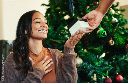 Christmas, hand with gift and woman with smile, couple and present exchange, surprise and happy to celebrate holiday. Christmas tree, love and care with box, celebration and festive tradition.