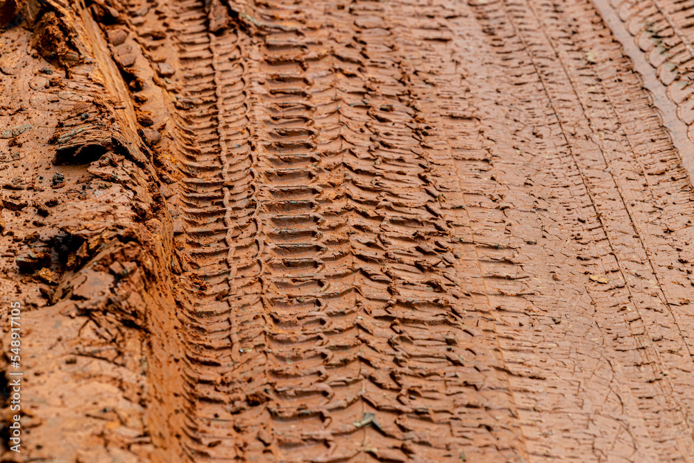Fototapeta premium Tire tracks from the wheels of passing cars in the wet, softened ground on a muddy rural road. Mult layers of tire tracks print on dirty red soil. Wheel marks of cars and trucks on countryside route.
