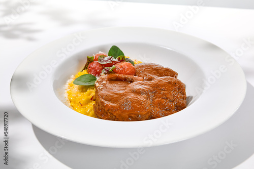 Traditional italian dish - osso buco with risotto milanese. Stew meat on bone with rice on white plate. Summer italian dining. Italian osso buco with garnish with hard shadows