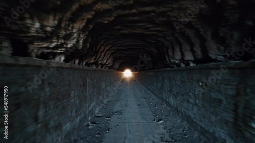 Inside the manmade channel structure of the famous Los Bermejales a reservoir in Arenas del Rey, province of Granada, Andalusia, Spain. with golden light glowing at end of tunnel