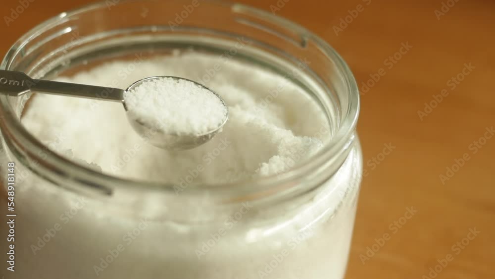 A teaspoon of table sea salt is being scooped with stainless steel measuring spoon cup