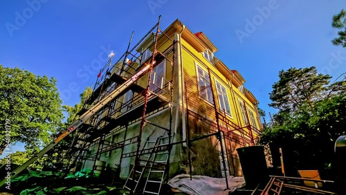 Time lapse of two people on scaffolding renovating the facade of a large detached house photo