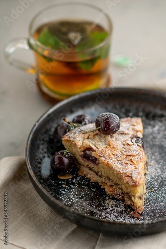 Slice of cherry cake on plate in background of tea