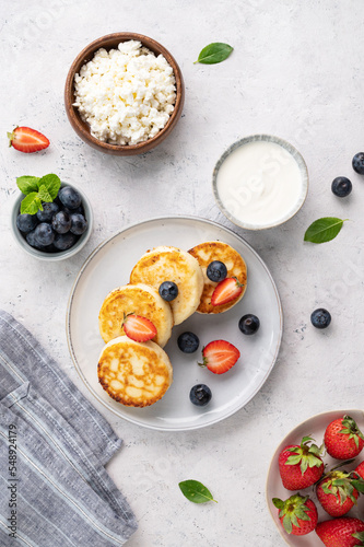 Flat lay pancakes with cottage cheese with fresh blerries and sour cream on a gray background. The concept of a healthy and delicious morning breakfast. Top view