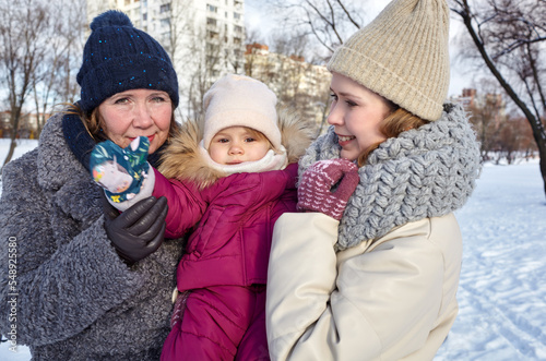 Grandmother, mother and daughter are walking in the winter city park on Christmas and New Year holidays. Parent and little child having fun outdoors