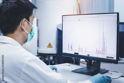 Scientist man checks the spectrum of sample analysis by nuclear magnetic resonance spectroscopy, NMR spectroscopy, as shown on a computer monitor in the laboratory.