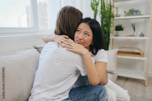 A man hugs his Asian woman friend at home. Psychological support for a friend