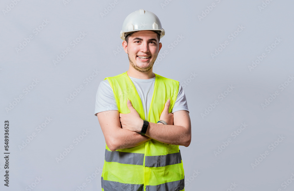 Portrait of smiling handsome engineer on white background, Portrait of young engineer wearing helmet and vest isolated. Young smiling engineer wearing helmet and vest with crossed arms isolated