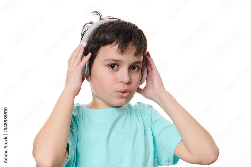Close-up portrait handsome multi-ethnic teenage boy in blue t-shirt, putting on wireless stereo headphones, looking at camera, isolated on white background, copy advertising space for promotional text Close-up portrait handsome multi-ethnic teenage boy in blue t-shirt, putting on wireless stereo headphones, looking at camera, isolated on white background, copy advertising space for promotional text