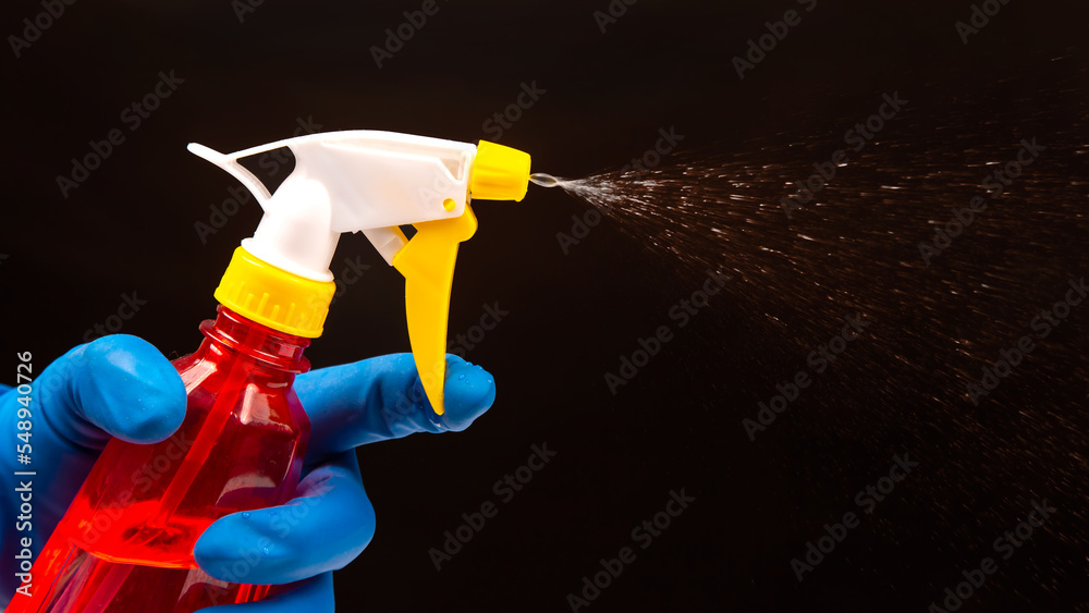 water sprayer bottle in a hand with gloves on a dark background with liquid spray. household items for home water sprayer bottle in a hand with gloves on a dark background with liquid spray. household items for home
