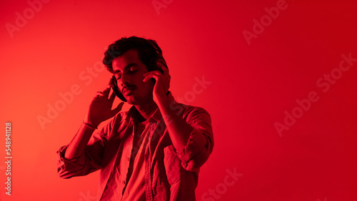 Obraz na plátně Young man listening to music isolated over red background, chilling and enjoying