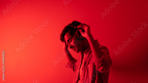 Young man listening to music isolated over red background, chilling and enjoying music, headphones music concept