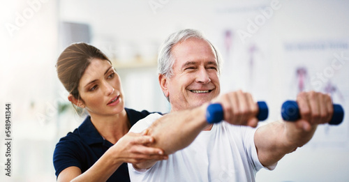 Physiotherapy, senior man and dumbbell exercise, injury rehabilitation or workout at health clinic. Happy elderly patient, woman physiotherapist or muscle training for strong body, care or fitness