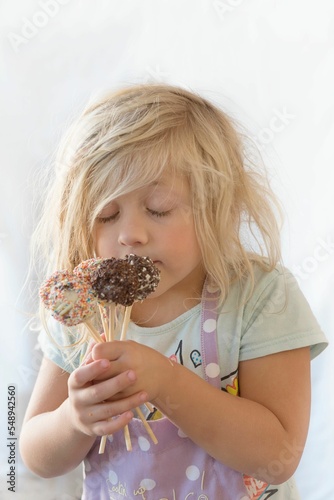 Vertical of a blonde child smelling the freshly baked sweets, lollipops