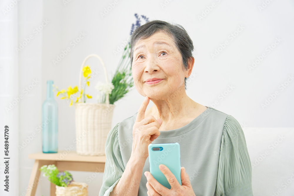 家でスマホを持って考える高齢者女性 家でスマホを持って考える高齢者女性