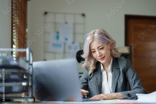 Portrait of a thoughtful Asian businesswoman looking at financial statements and making marketing plans using a computer on her desk