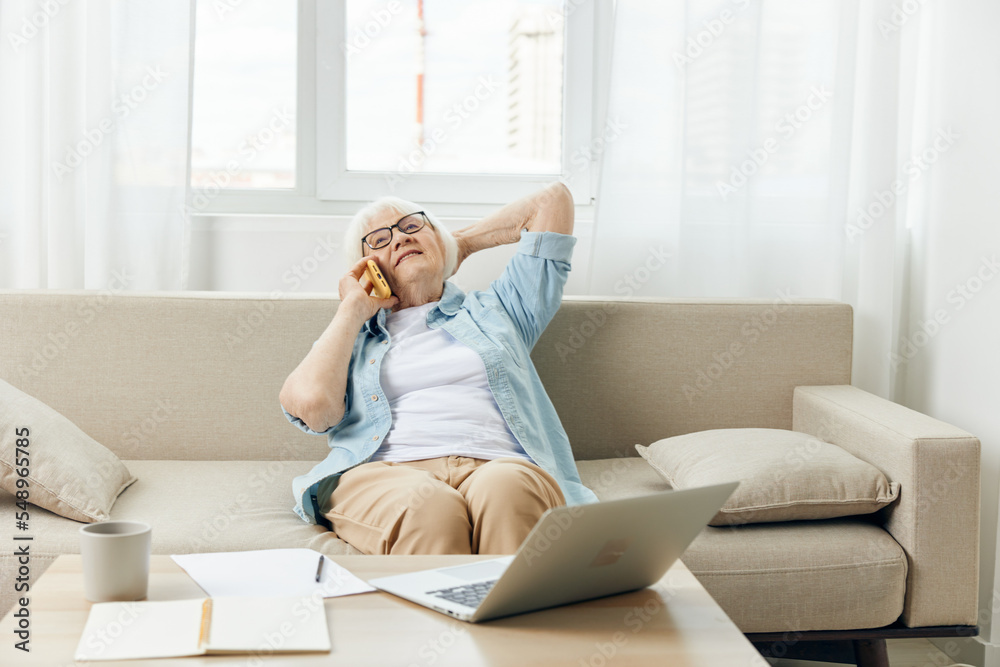 a happy, relaxed elderly lady works from home sitting on a cozy sofa in a bright interior and talking on the phone with her hand behind her head a happy, relaxed elderly lady works from home sitting on a cozy sofa in a bright interior and talking on the phone with her hand behind her head
