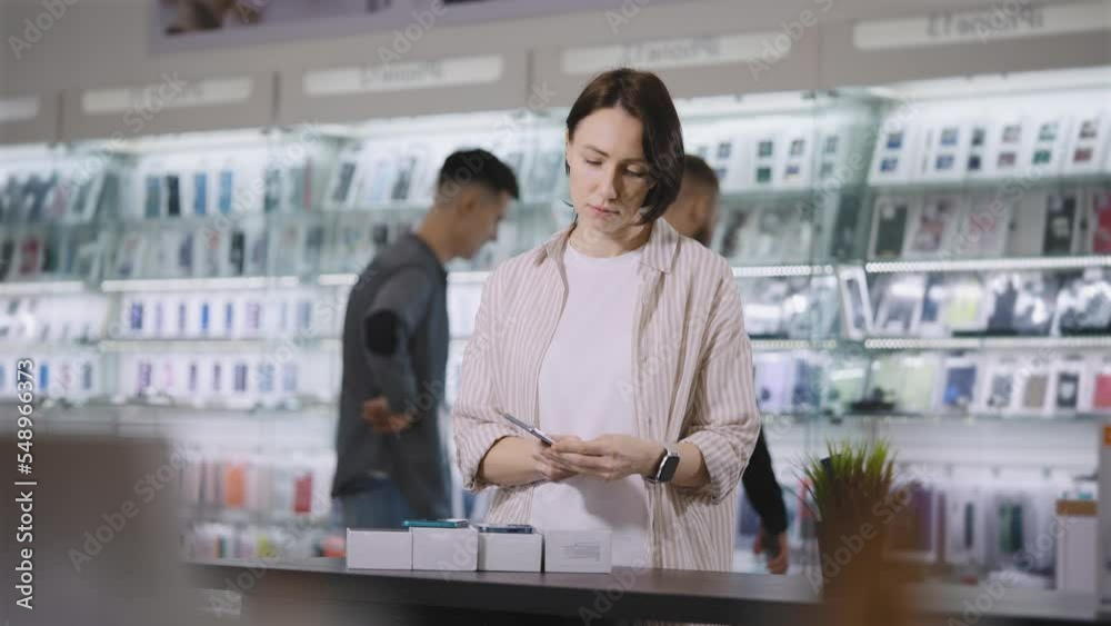 At the gadget store. A woman chooses a new smartphone, compares design and features. At the gadget store. A woman chooses a new smartphone, compares design and features.