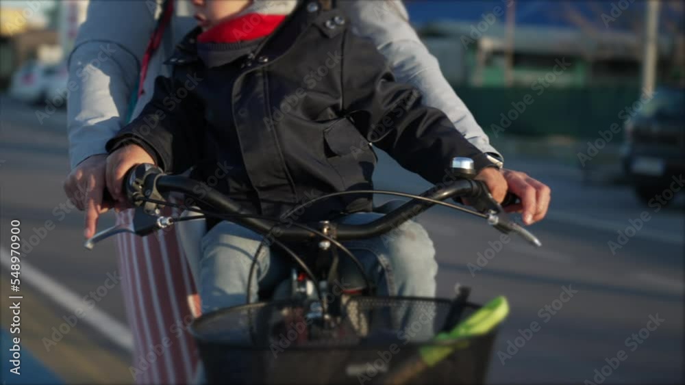 Mother riding bicycle with child seated in front. Parent and kid wearing winter clothes jacket scarf and beanie in bike lane Mother riding bicycle with child seated in front. Parent and kid wearing winter clothes jacket scarf and beanie in bike lane