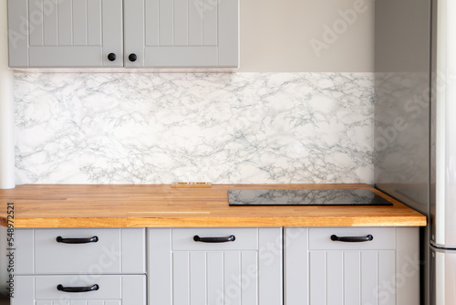 Empty modern minimal grey color kitchen, marble wall, solid natural wood butcher block countertop with built in small stove, black handles.