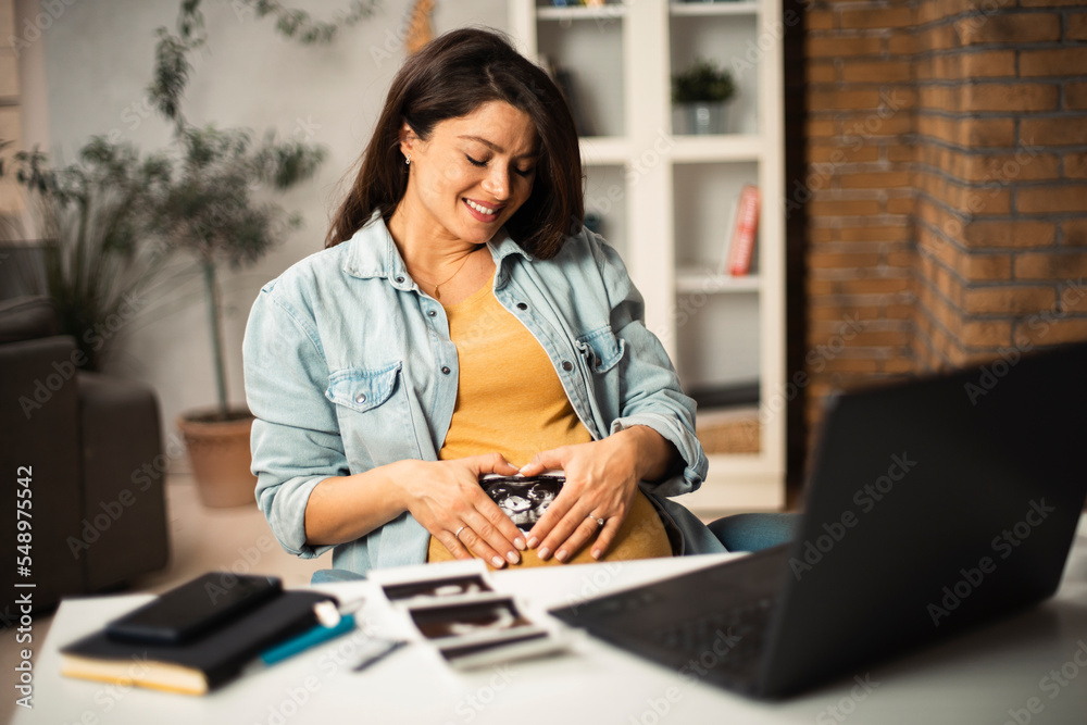 Beautiful young pregnant woman looking at ultrasound pictures of her baby. Businesswoman in office.