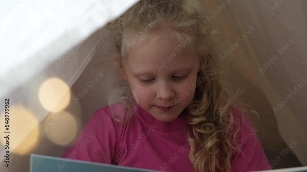 cute toddler girl playing in a tent at home, wigwam made of sheets, a child in a blue santa hat waiting for christmas, advent concept, bokeh light bulbs cute toddler girl playing in a tent at home, wigwam made of sheets, a child in a blue santa hat waiting for christmas, advent concept, bokeh light bulbs