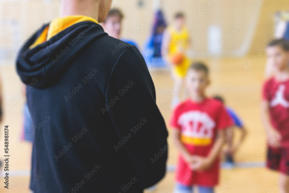 Junior young basketball team with a coach, group of kids children team having training and team talk speach with trainer instructor, basket coach explaining the game plan tactics on coach's clipboard