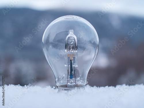 Close-up of a light bulb sticking up from soft snow with a blurred winter landscape in the background