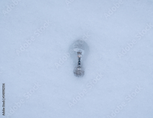 Light bulb laying in the white snow while turned of.