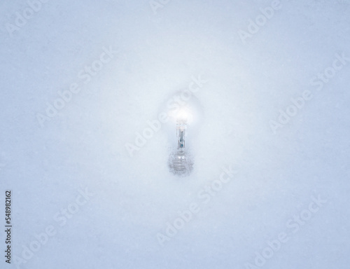 Shining Light bulb laying in the white snow while illuminating its surroundings.