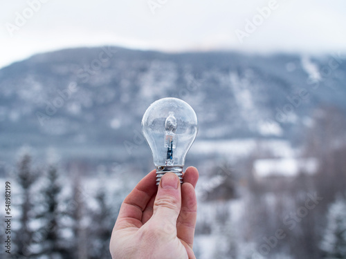 Hand holding a lightbulb up in front of a snowy mountain landscape