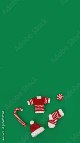 decorative knitted ornaments sock, sweater, hat and caramel in red and white color on green background, vertical, 16:9