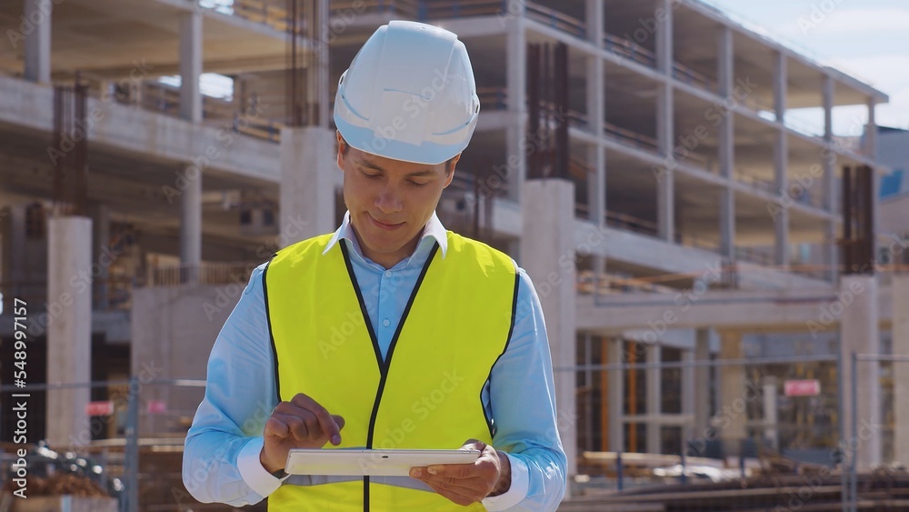 Professional builder standing in front of construction site. Foreman in hardhat helmet and vest. Office building and crane background. Business, real estate and investment. Professional builder standing in front of construction site. Foreman in hardhat helmet and vest. Office building and crane background. Business, real estate and investment.
