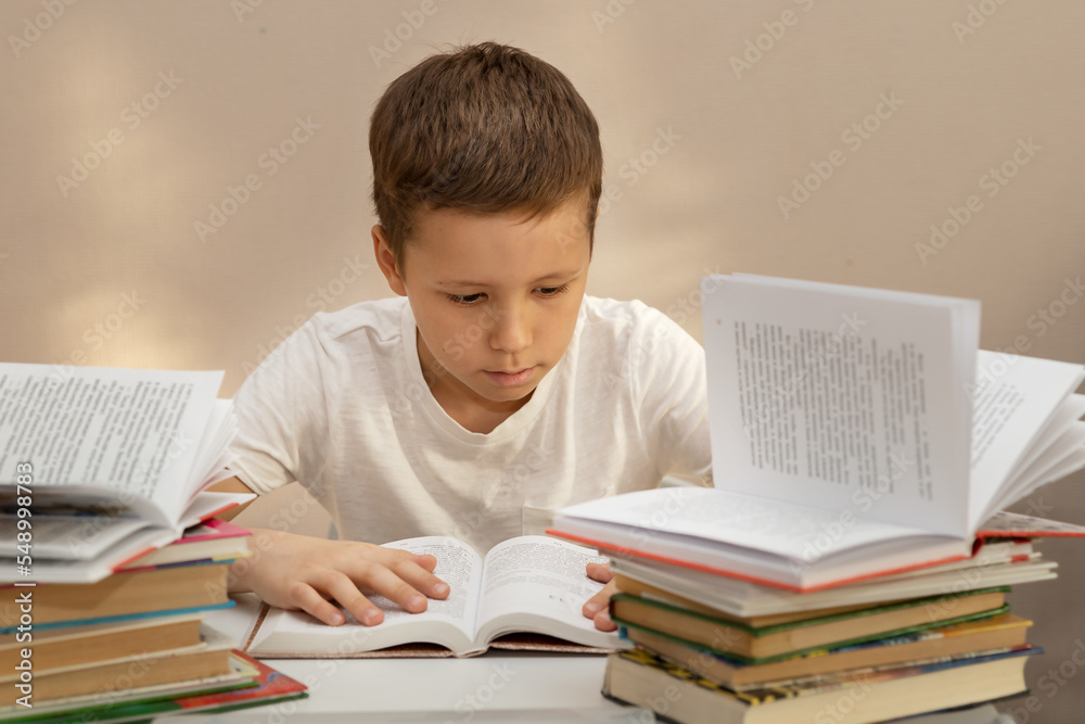 A 10-year-old boy carefully reads and studies at a table with piles of books A 10-year-old boy carefully reads and studies at a table with piles of books