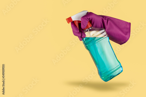 Purple cleaning glove floating in the air on yellow background holding desinfectant spray photo