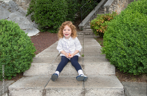 Fototapeta Bambina bionda con riccioli d'oro che ride seduta sulle scale
