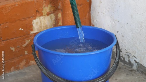 Clear water flows from a hose into a blue bucket. Water is poured into a bucket