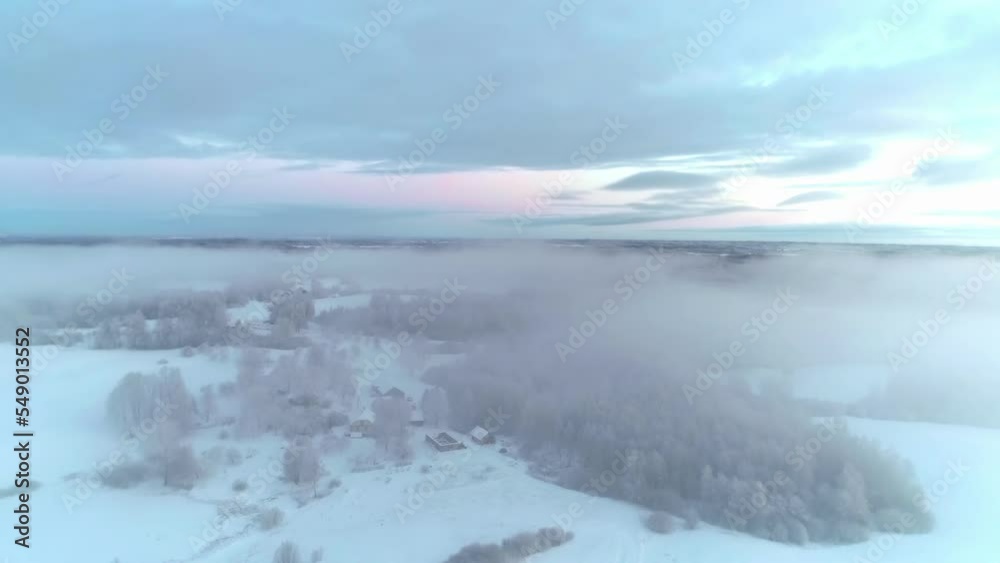 Aerial drone shot flying above the picturesque countryside covered in fresh powder snow through white clouds during evening time. Aerial drone shot flying above the picturesque countryside covered in fresh powder snow through white clouds during evening time.