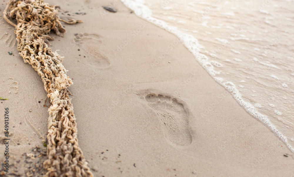 Fußspuren im Sand neben angeschwemmten Fischernetz.
Footprints in the sand next to washed up fishing net.