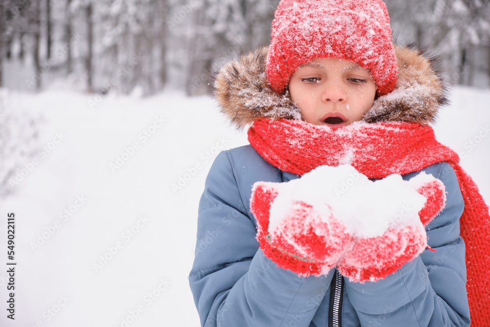 a teenage girl is blowing on the snow in her palms and fanning, mittens and a knitted hat, changing weather a teenage girl is blowing on the snow in her palms and fanning, mittens and a knitted hat, changing weather