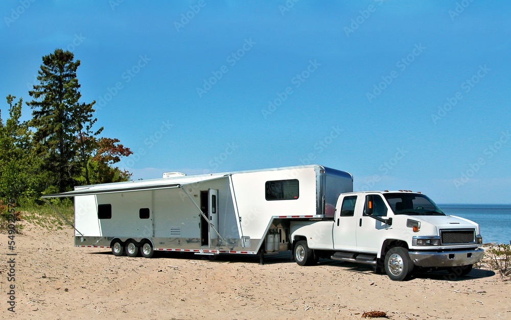 White toy hauler travel trailer camping on the sandy shore of lake Superior