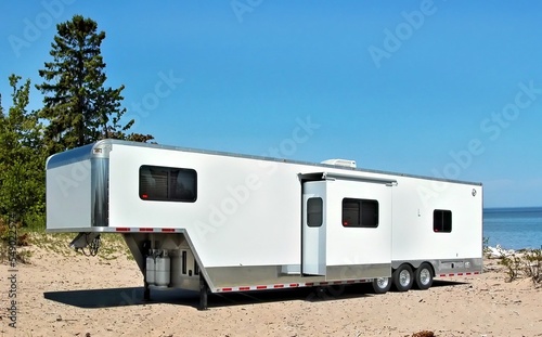 White toy hauler travel trailer camping on the sandy shore of lake Superior