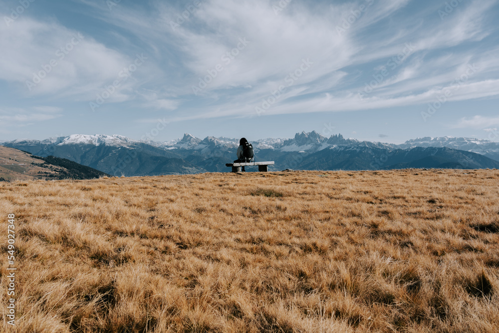 Eine Frau sitzt auf einer kleinen Bank in den Bergen und betrachtet die Dolomiten in der Ferne. Latzfonz 1