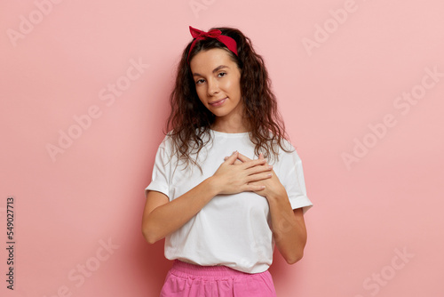 Obraz na plátně Young woman puts hands on the chest, isolated over pink background