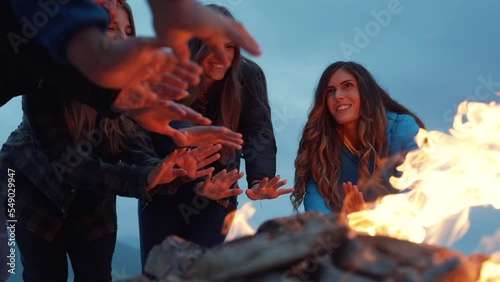 Group of friends having fun together at night party around bonfire - Friendship life style concept with happy people traveler making themselves warm by campfire at dusk night time