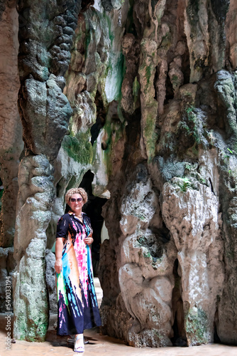 A pretty woman in a long colored dress against a background of colorful rocks in Batu Caves in Gombak, Selangor, Malaysia
