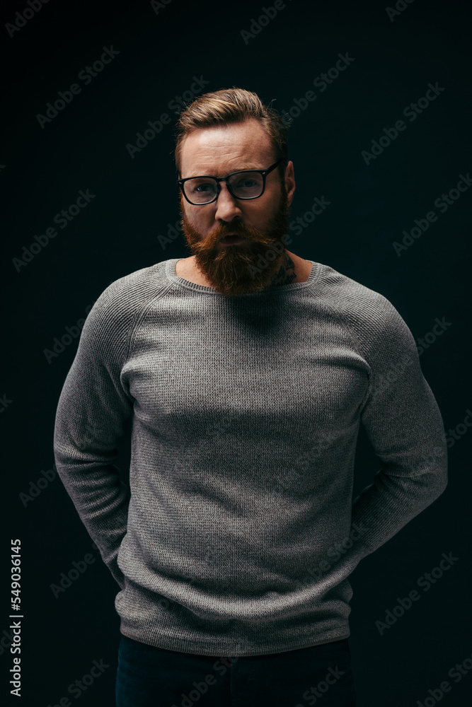 Portrait man in eyeglasses and grey jumper looking at camera isolated on black.